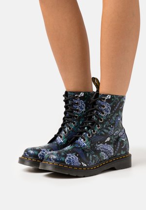 Schwarze Stiefel mit Blumenmuster, die blaue und grüne botanische Designs zeigen. Schnürstil mit gelben Nähten und Gummisohle.