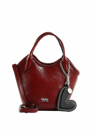 Sac à main en cuir rouge avec deux anses, logo DKNY Jeans argenté et breloque noire en forme de cœur avec des clous argentés sur une chaîne.