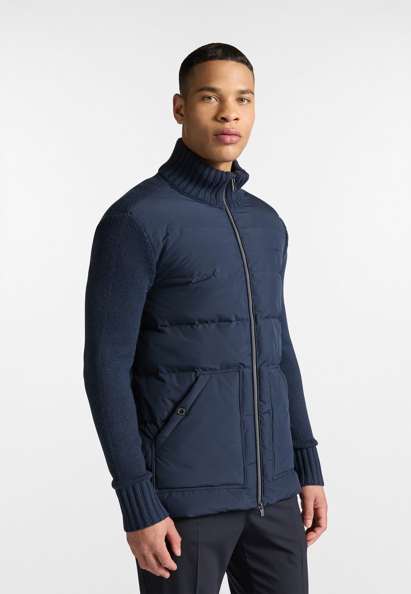Giacca puffer navy con maniche a costine e colletto alto. Presenta una chiusura a zip, dettagli texturizzati e tasche frontali.