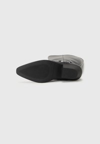 Botín negro hasta el tobillo con punta afilada, parte superior de cuero liso, hebilla decorativa y suela de goma texturizada para un mejor agarre.