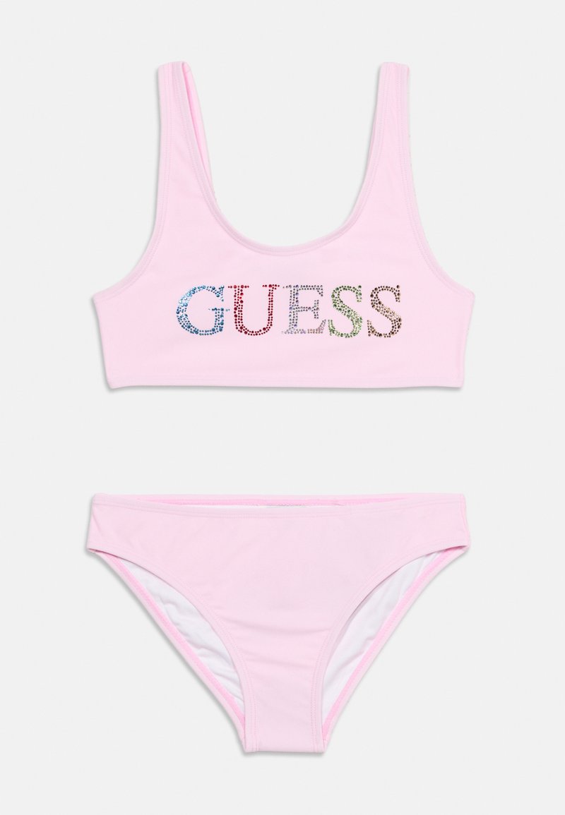 Maillot de bain deux pièces rose clair avec un crop top présentant le logo "GUESS" en strass multicolores et un bas de bikini assorti.