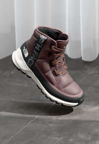 Lila és fekete bokacsizma párnázott szintetikus felsőrésszel, gumitalppal és kontrasztos fűzőkkel. Az oldalon a The North Face logó található.