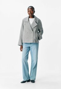 Veste double boutonnage en chevrons gris avec de grands boutons, associée à un jean taille haute bleu clair et des bottines noires à talons.