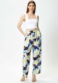 White cropped tank top with a square neckline, paired with wide-leg trousers featuring a colorful abstract pattern of blue, yellow, and black.