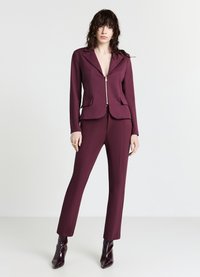 Completo su misura color borgogna con giacca aderente con zip e due tasche frontali, abbinato a pantaloni slim-fit. Tessuto dalla texture liscia.