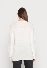 Leichter weißer Pullover mit lockerer Passform, weiten Ärmeln und einer dezenten Rippstruktur, von hinten gegen einen schlichten Hintergrund präsentiert.