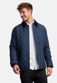 Navy quilted jacket with a soft collar, featuring a zippered front and pockets. Smooth texture with diamond patterns on the fabric.