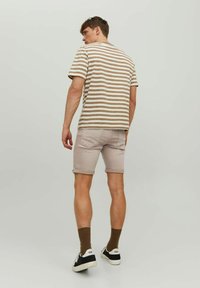 Camiseta de manga corta a rayas en tonos beige y crema, de corte relajado; combinada con pantalones cortos de color beige claro. Lleva zapatillas de deporte en blanco y negro y calcetines marrones.