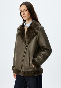 Brązowa kurtka z owczej skóry z dużym futrzanym kołnierzem, na zamek, z bocznymi kieszeniami i detalami przy rękawach o prążkowanej strukturze. Teksturowana skórzana część i miękka podszewka.