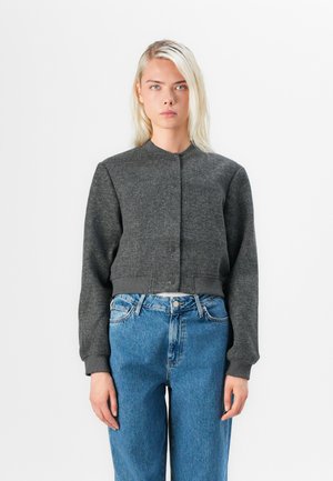 Dark gray cropped bomber jacket with a round neck, front buttons, and ribbed cuffs, paired with high-waisted denim jeans.