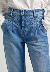 I jeans a vita alta di colore azzurro chiaro presentano un design plissettato, chiusura con doppio bottone e tasche. Realizzati in denim con una texture morbida.