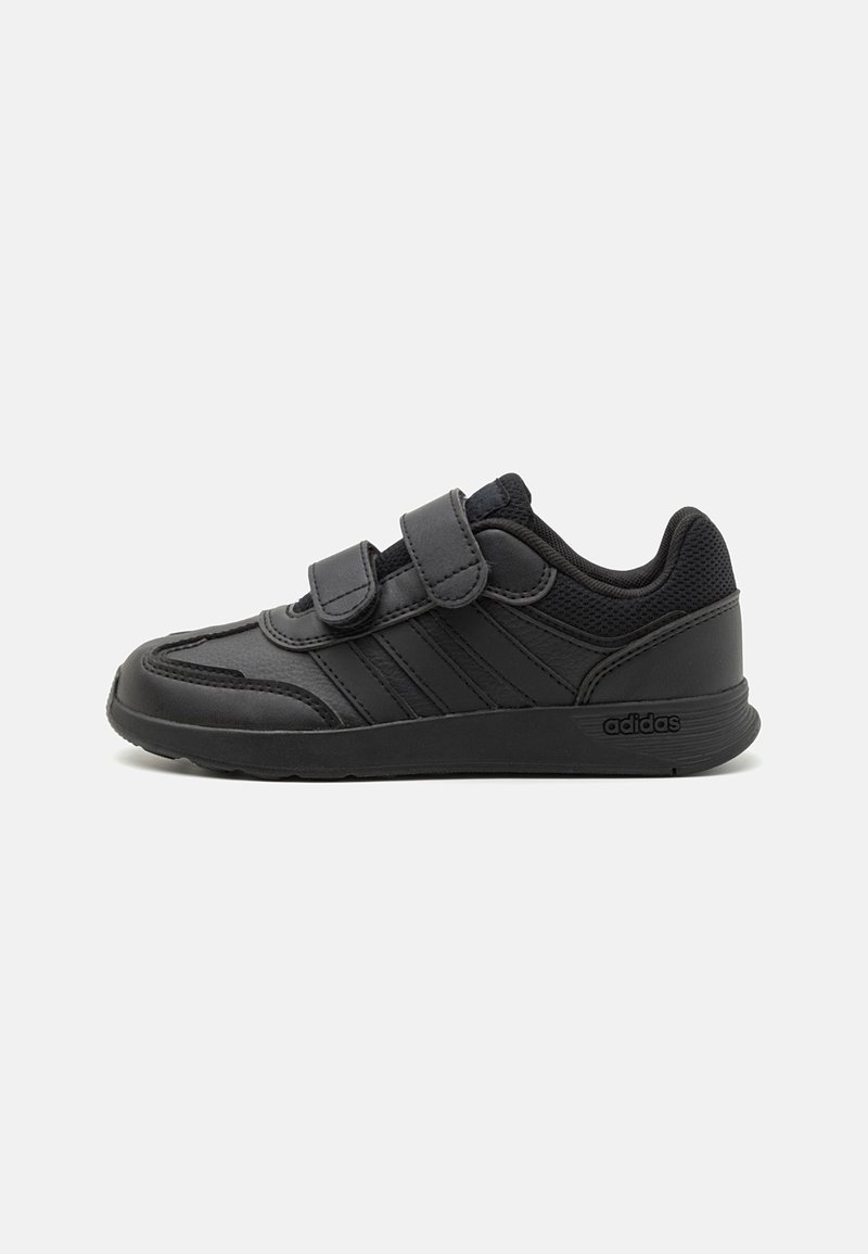 Chaussure de sport noire avec une tige synthétique lisse, des accents en mesh, deux brides en Velcro et une semelle en caoutchouc. Présente trois bandes latérales.