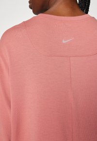 Nahaufnahme einer Person, die einen pinken Nike-Sweatshirt trägt, die Rückennaht mit abgesteppten Nähten und kleinem reflektierendem Nike-Logo zeigt.