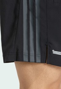 Pantalones cortos deportivos negros con tres rayas verticales grises, con aberturas en el dobladillo y un logo "Climalite" en el costado. Textura suave.