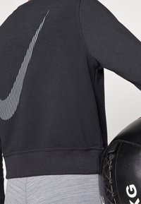 Sweat-shirt noir avec un logo Nike stylisé et texturé en rayures blanches, doté d'un ourlet côtelé. Pantalon gris ajusté et un medicine ball noir inclus.
