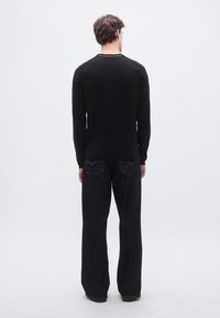 Pitkähihainen musta paita pyöreällä kaula-aukolla, yhdistetty tummansinisiin leveälahkeisiin farkkuihin, joissa on takatasku. Kokonaisuudessaan sileä pinta.