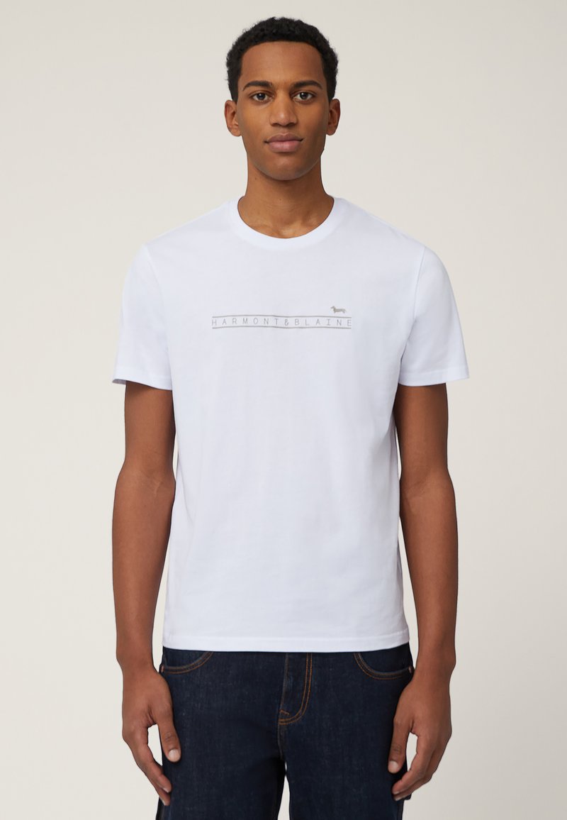 White cotton t-shirt with short sleeves, featuring a central gray logo design "HARMONT & BLAINE" and a small animal icon above.