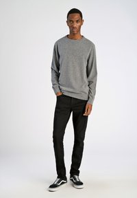 Grauer Pullover mit runder Ausschnitt, langen Ärmeln; kombiniert mit schwarzen Jeans und schwarz-weißen Sneakers. Glatte Textur, lässige Passform.