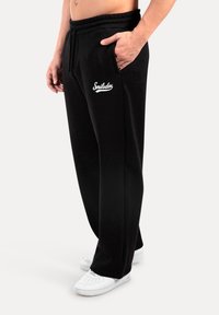 Pantalones deportivos negros con cintura elástica y bolsillos laterales, con el logo blanco de "Smilodox". Textura suave y diseño de piernas ajustadas.