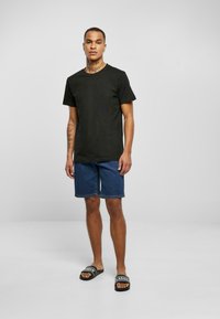 T-shirt en coton noir, short en denim bleu et sandales à slides noires avec des lettres blanches. Design simple et coupe décontractée. Pas de motifs ni d'accents.