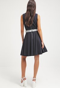 Abito senza maniche di colore blu navy con gonna svasata, dotato di una cintura bianca con motivo e chiusura posteriore con zip. Tessuto liscio con una silhouette strutturata.