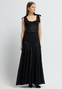 Sort blonde maxi kjole med en tætsiddende overdel, firkantet udskæring og skulderbånd. Den udskårne nederdel har detaljerede blonde mønstre og lag.