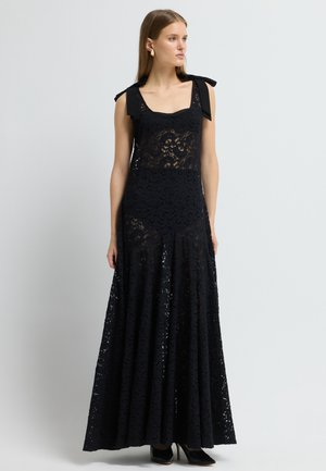 Svart maxiklänning i spets med en figurnära överdel, fyrkantig halsringning och axelband. Utsvängd kjol med intrikata spetsmönster och flera lager.