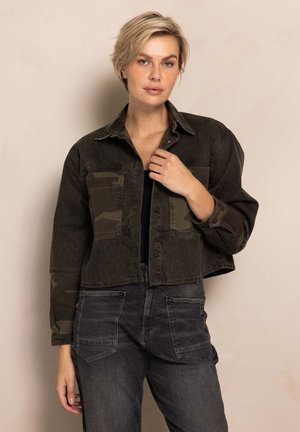 Cropped dark green denim jacket with leopard and camo patterns, button closure, and chest pockets, paired with gray cargo pants.