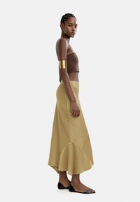 Brązowy dopasowany crop top, złota bransoletka i beżowa spódnica do kolan z zaokrąglonym dołem. Całość uzupełniają czarne sandały na płaskiej podeszwie.