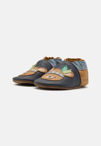 Chaussures en cuir pour tout-petits en bleu marine et tan avec un motif d'ours, présentant des accents de feuilles vertes et une semelle douce et flexible.