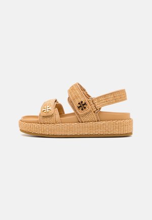 Beige vævet platformsandal med to justerbare remme og sort-guld logoaccenter på hvid baggrund.