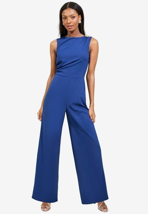 Mono azul con un cuerpo ajustado y piernas anchas. Presenta un diseño drapeado y un acento de un solo hombro. Fabricado con tela suave.