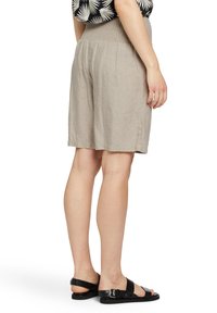 Pantalones cortos de lino beige con cintura fruncida, hasta la rodilla, con un corte relajado y bolsillos laterales, combinados con sandalias negras de tiras.