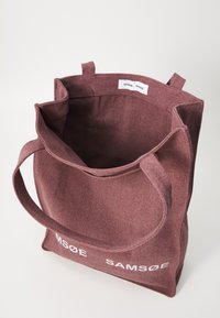 Bordeaux fargett stoffトートバッグ med robuste håndtak, som har en stor åpning og innvendige merker som viser "SAMSØE SAMSØE." Enkel design og tekstur.