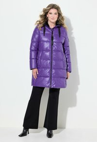 Abrigo de plumas morado con acabado brillante, diseño acolchado, cremallera frontal, acentos negros y capucha. Combinado con pantalones acampanados negros y botas.