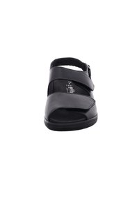 Black sandal featuring an open toe, curved straps across the foot, and a buckled ankle strap. Smooth leather material with a flat sole.