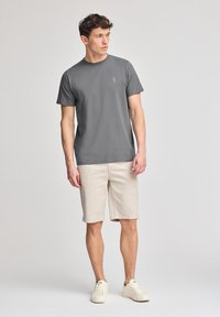 Grå bomullströja med rund halsringning, i kombination med beige shorts och ljusa sneakers. Enkel design med en liten logotyp på bröstet.