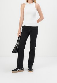 Canotta bianca a costine, jeans di denim neri, sneakers neri con strisce bianche, porta una piccola borsa nera; outfit casual e alla moda.