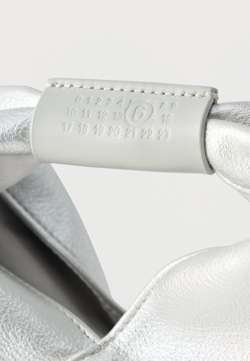 Chaussure en cuir argenté avec une étiquette cousue montrant des numéros embossés de 0 à 23, le numéro 6 étant encerclé.