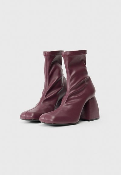 Bottines bordeaux en cuir lisse avec un design froncé, bouts carrés et talons épais. Fini texturé pour un intérêt visuel.