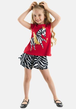 Red sleeveless top featuring a zebra graphic with gold accents, paired with black and white zebra print ruffled shorts. Black flat shoes.