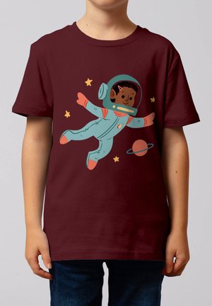 Kind trägt ein bordeauxrotes Hemd mit einer Illustration eines lächelnden Astronauten, der in der Nähe von Sternen und einem ringförmigen Planeten schwebt.