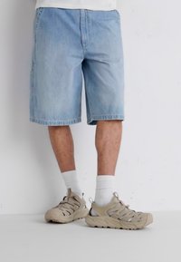 Jasnoniebieskie szorty dżinsowe o luźnym kroju, z postrzępionym dołem i widocznymi detalami przeszyć, w połączeniu z beżowymi trampkami i białymi skarpetkami.