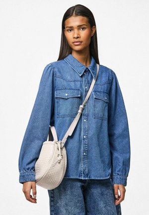 Camicia di jeans con maniche lunghe, chiusura con bottoni e due tasche sul petto; abbinata a una borsa intrecciata di colore chiaro con tracolla.