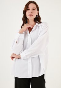 Hvid bluse med en afslappet pasform, knaplukning fortil og lange ærmer. Med slids i ærmekanterne og en buet kantdesign.
