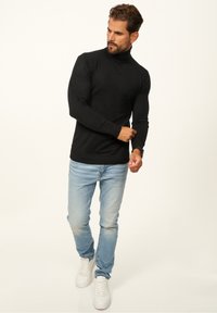 Black turtleneck sweater in a fitted design, paired with light blue jeans and white sneakers. The sweater features ribbed cuffs and hem.