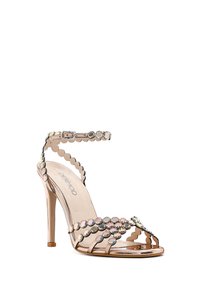 Rose gold high-heeled sandal with ankle strap, decorated with iridescent round studs and scalloped edges.