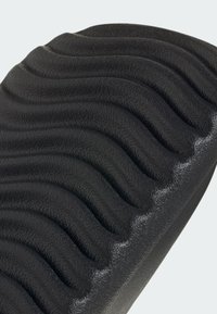 Black rubber mat featuring a wave pattern with a textured surface. Curved edges and a smooth base provide stability and grip.