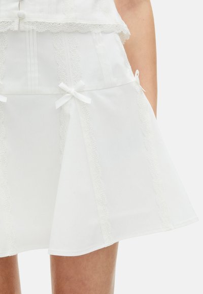 Jupe blanche en tissu léger avec des bordures en dentelle, des accents en forme de nœud et un design évasé. Présente des rayures verticales et une taille bien définie.