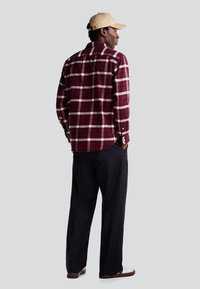 Camicia in flanella a quadri rossi e bianchi con maniche lunghe e polsini a bottone, abbinata a pantaloni a gamba larga a strisce blu navy e un berretto beige.